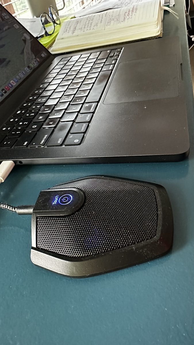 Hermes Ear, the AI meeting assistant device, on Rea Hailley's desk beside her laptop