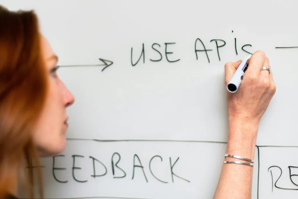 Woman writing USE APIs on whiteboard discussing custom software for startups